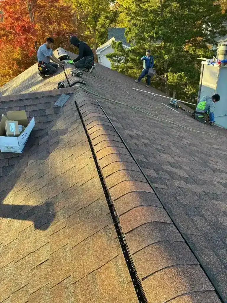 Four roofers installing a ridge vent along the peak of a residential asphalt shingle roof