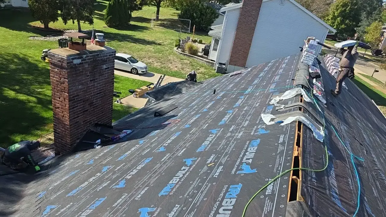 Roofers installing TruBuilt underlayment on a residential roof in St. Louis with brick chimney visible