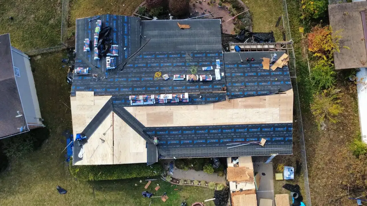 Aerial drone view of residential roof replacement in progress with underlayment and shingle bundles staged on roof deck.