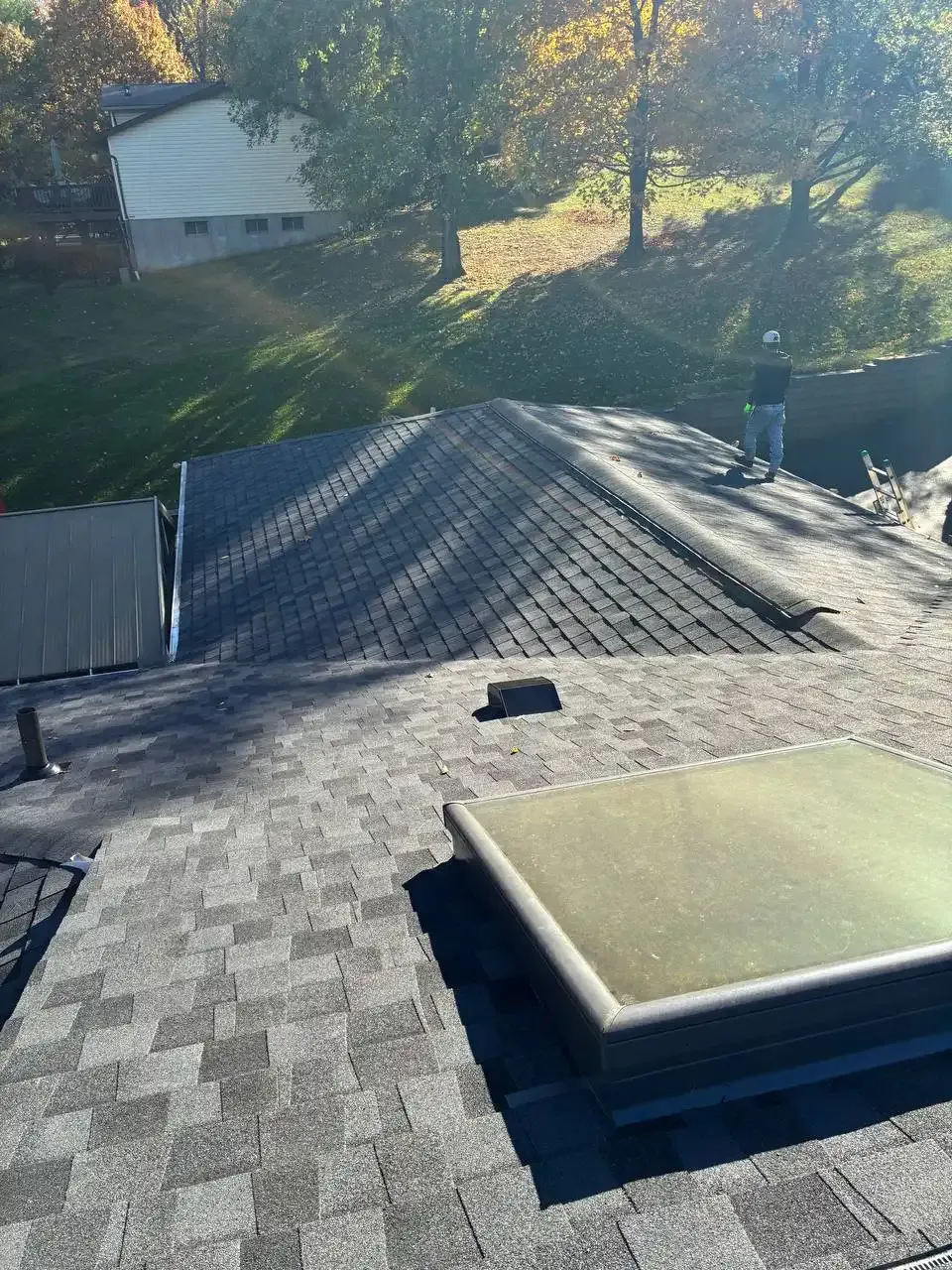 Roofing contractor in hard hat standing on newly installed asphalt shingle roof in St. Louis, MO