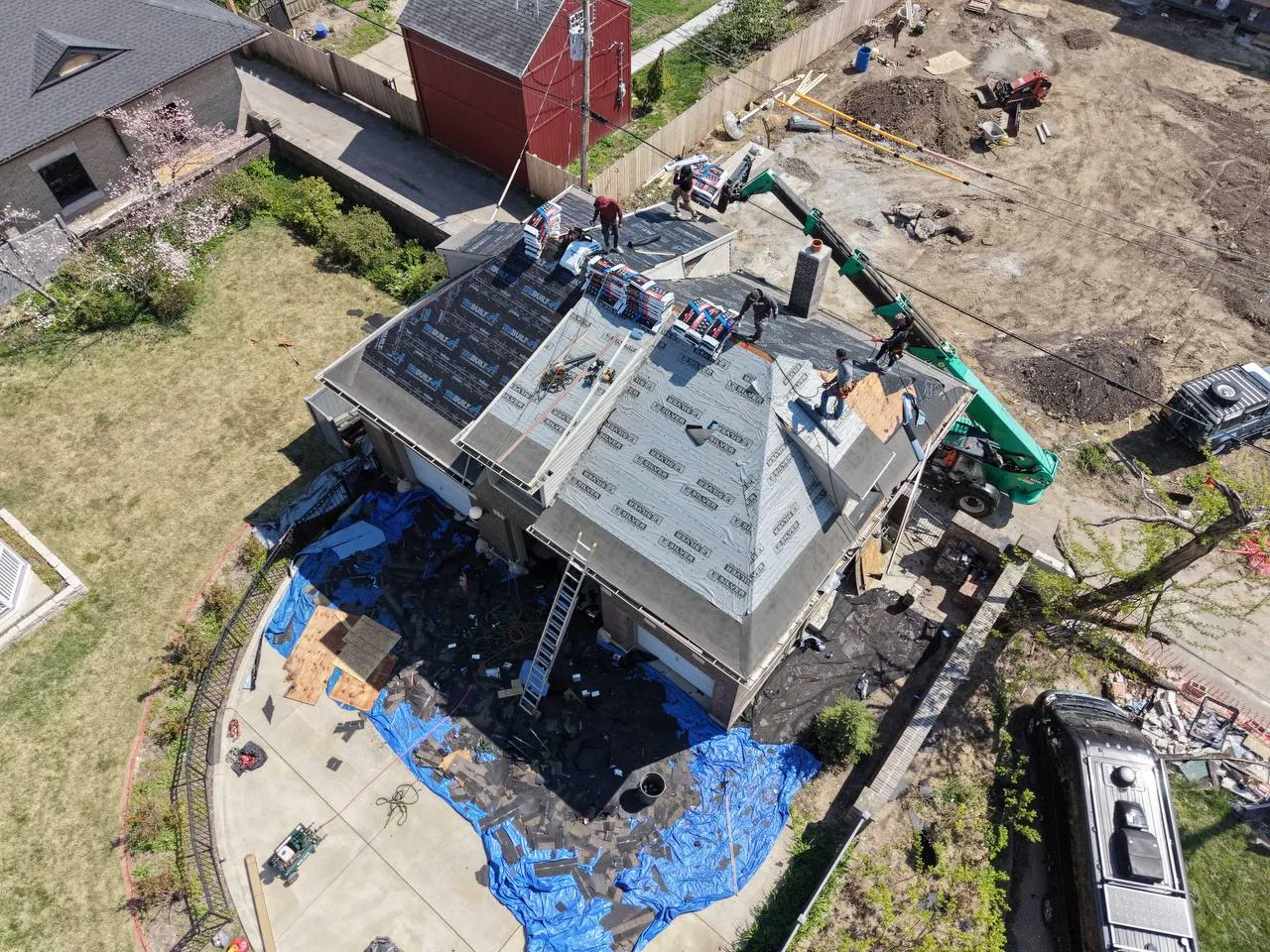 Aerial drone view of active roof replacement on St. Louis home with crew, shingles, and crane lift equipment.