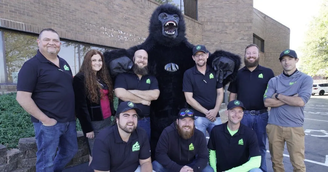 Gorilla Roofing team of 9 employees posing with a gorilla mascot costume outside brick building