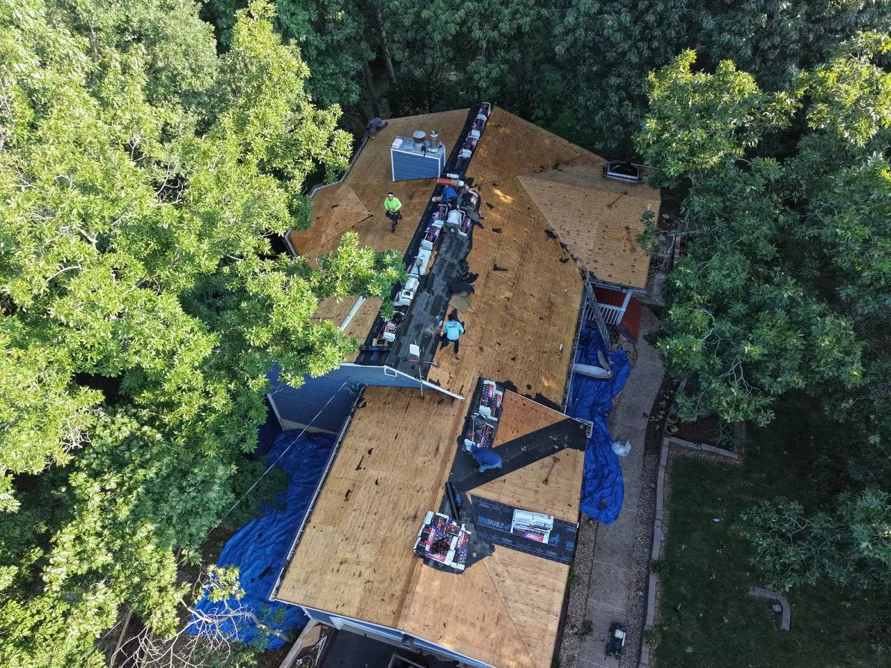 Aerial drone view of a home in St. Louis MO with old shingles stripped, showing bare wood decking during roof replacement.