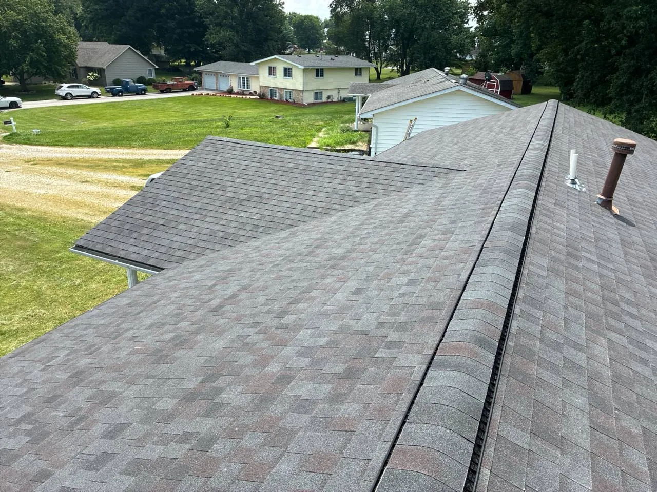 Aerial view of newly installed gray asphalt shingle roof with ridge vent and pipe boots on a residential home.