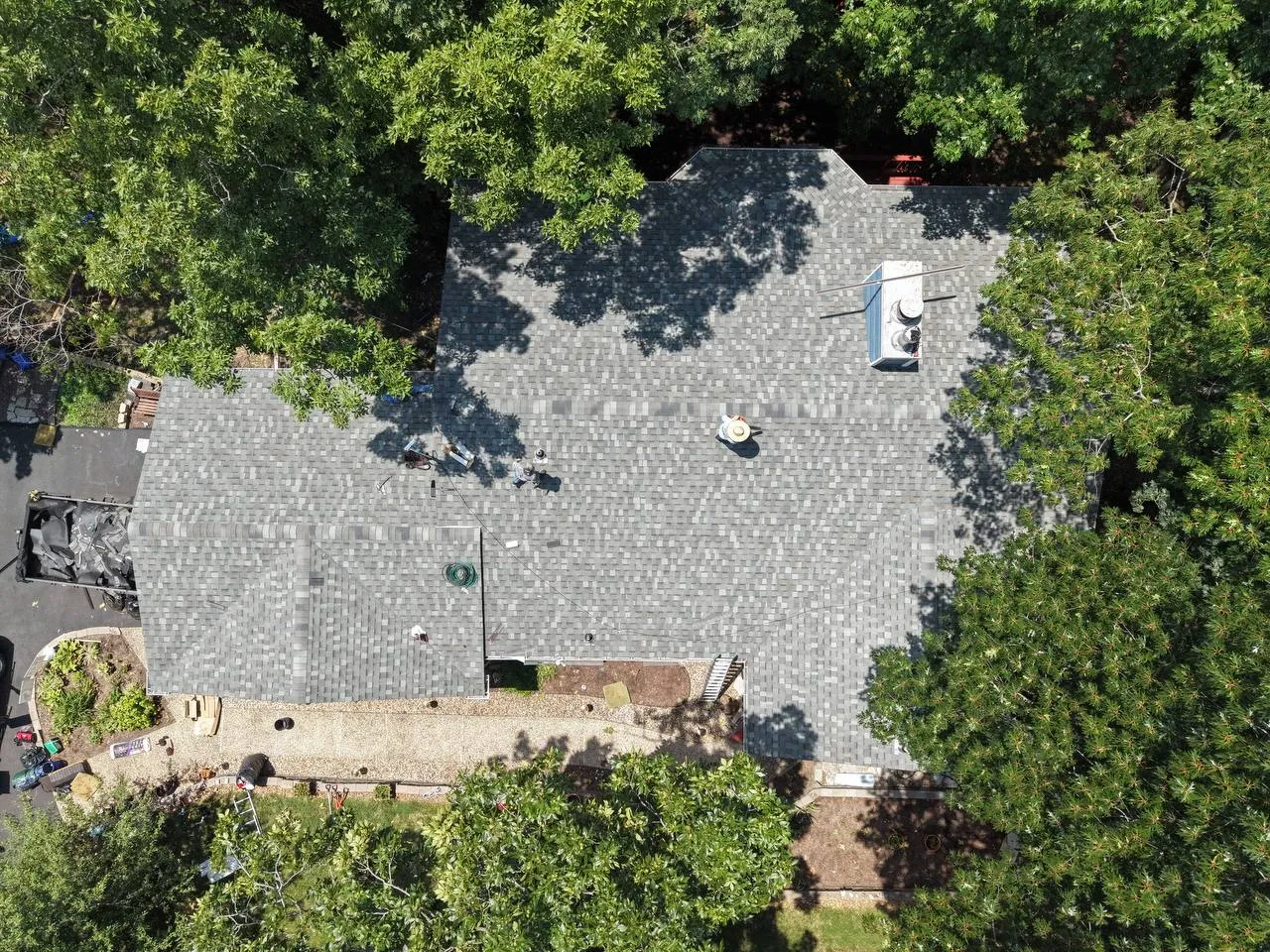Aerial drone view of a large residential roof with gray asphalt shingles being inspected by workers in St. Louis, MO.