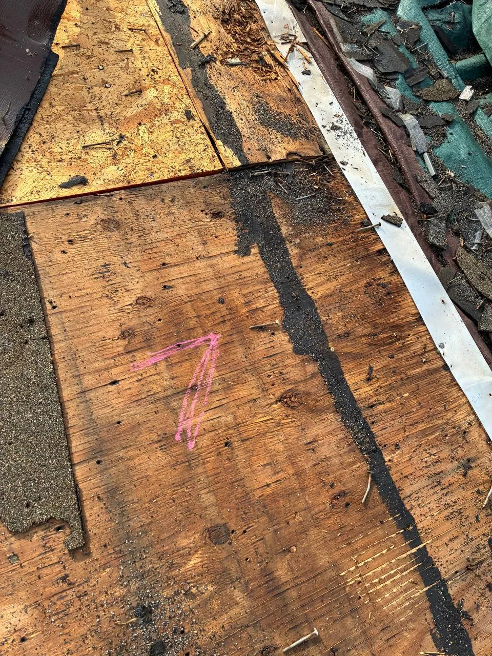 Exposed roof decking during tear-off showing old sheathing, black sealant streak, and pink spray-painted number 7.