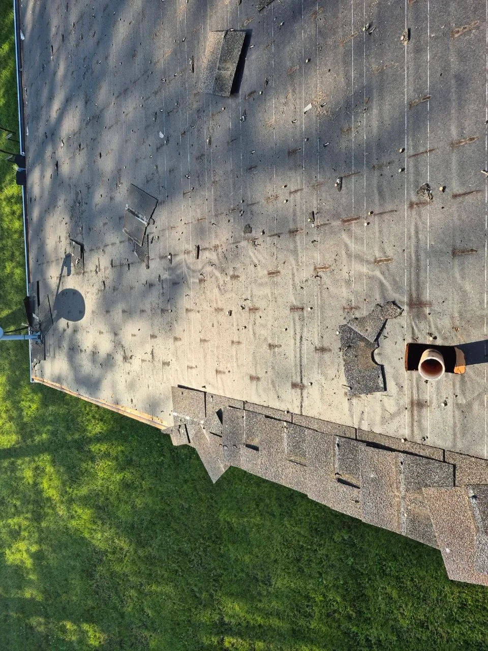 Aerial drone view of a severely storm-damaged residential roof with missing shingles and exposed underlayment in a Wildwood, MO neighborhood