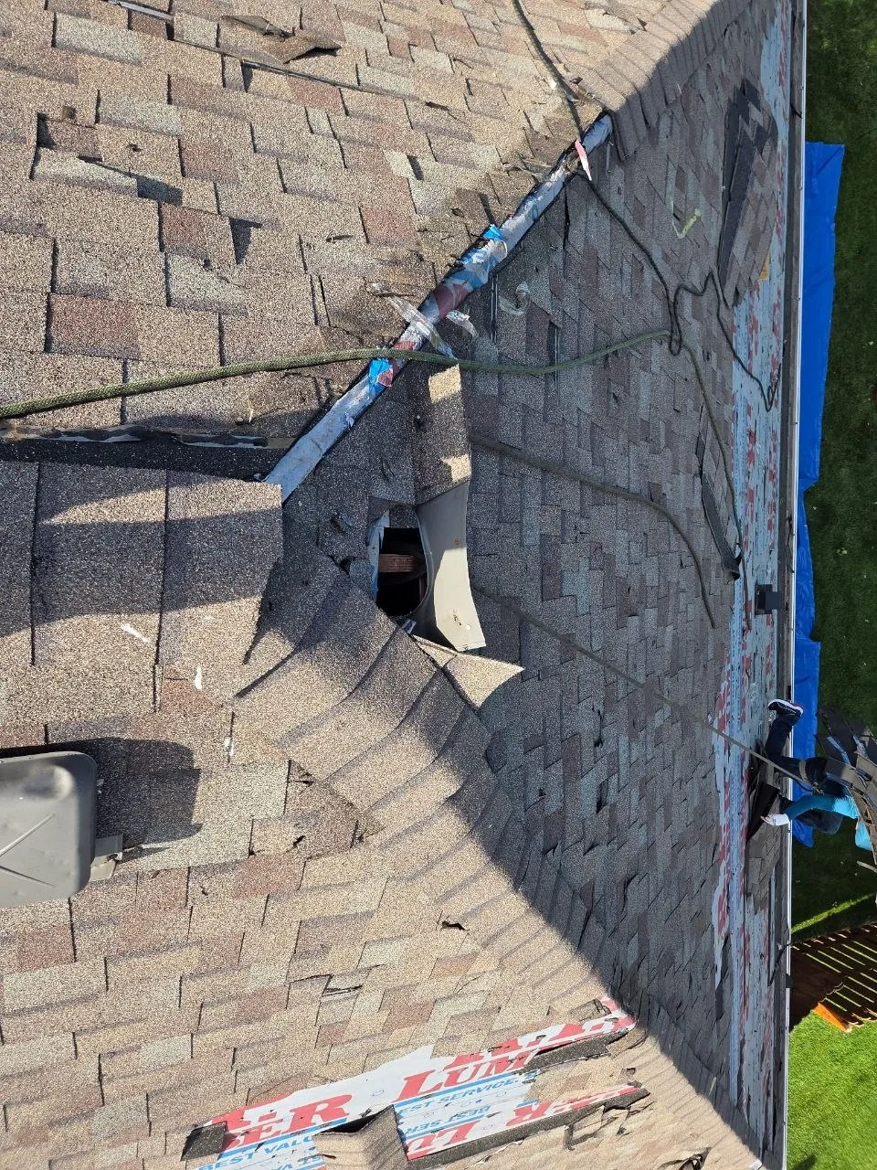 Aerial view of a severely storm-damaged roof with large hole and torn shingles on a Chesterfield, MO home