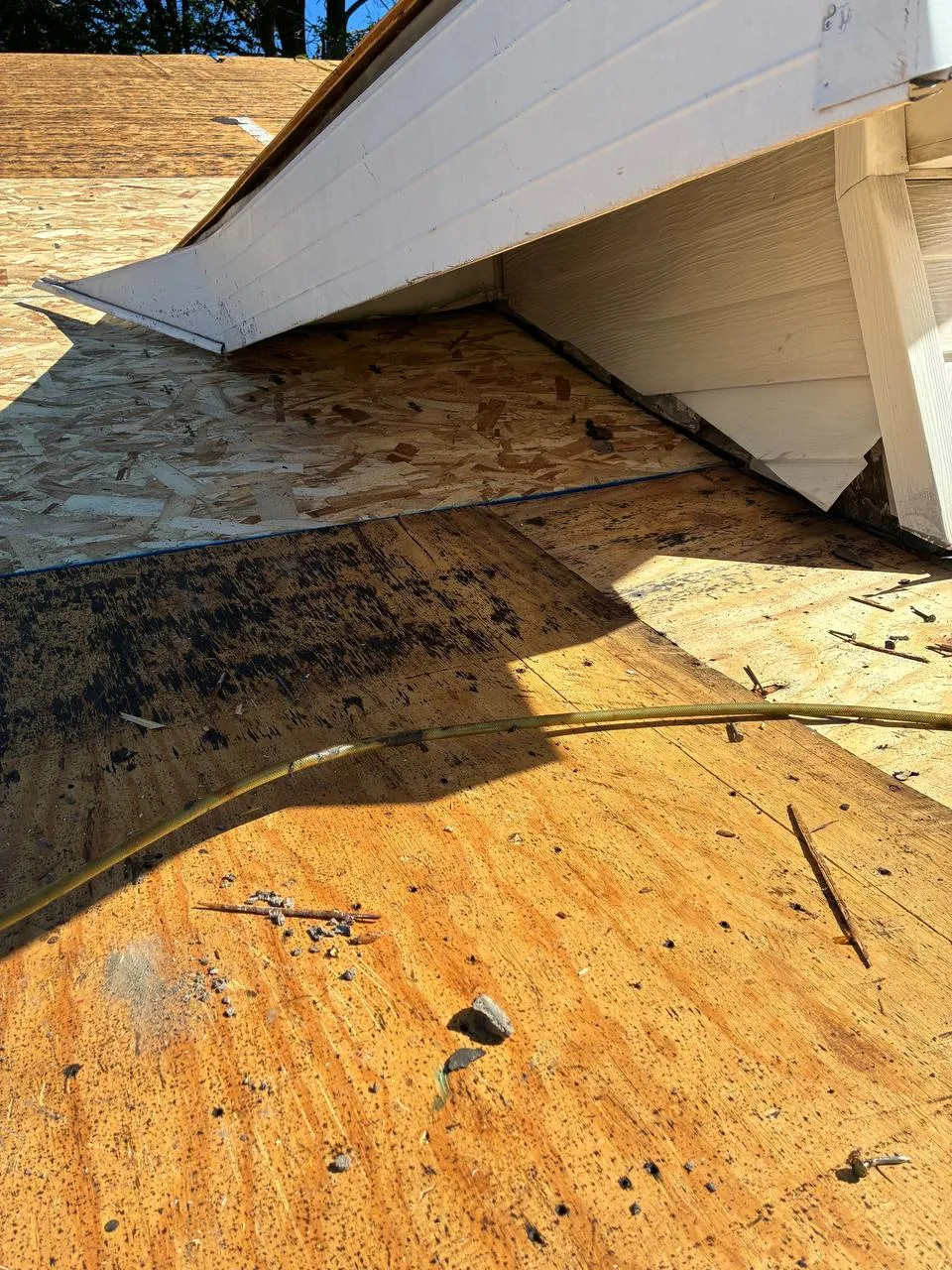 Old roof decking with dark moisture and mold staining next to new OSB sheathing below a dormer during a roof replacement.
