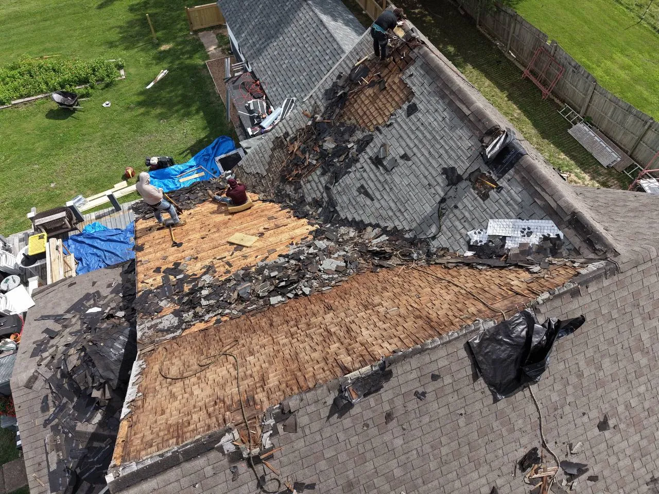 Aerial view of a St. Louis home mid-reroof with shingles stripped, exposing wood decking as workers complete tear-off.