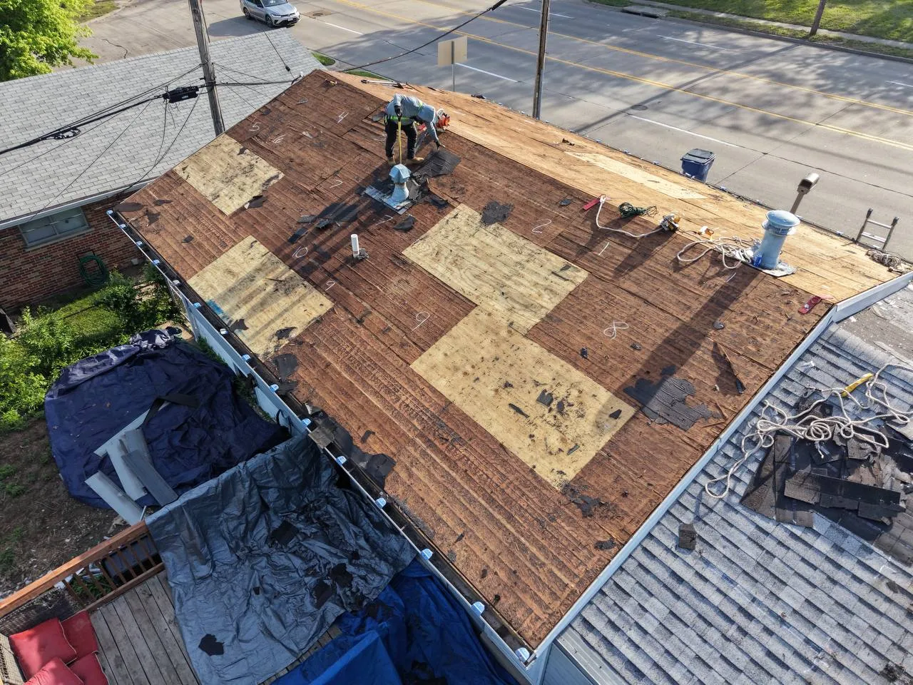 Roofer inspecting a residential roof deck where old shingles have been stripped away, showing granule loss and wear.