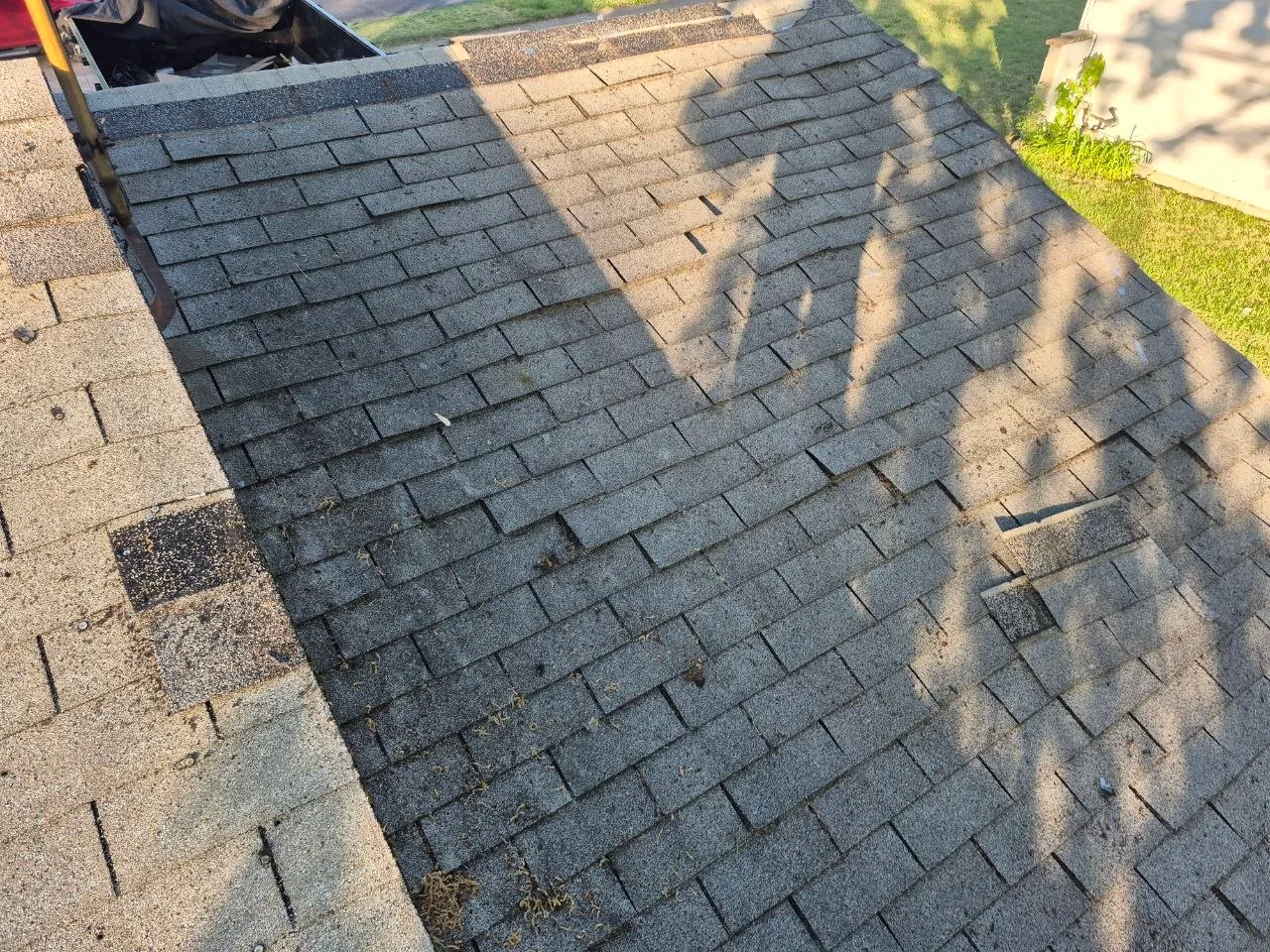 Worn and curling asphalt shingles with granule loss on a residential roof, consistent with wind damage pattern on a St. Louis home.