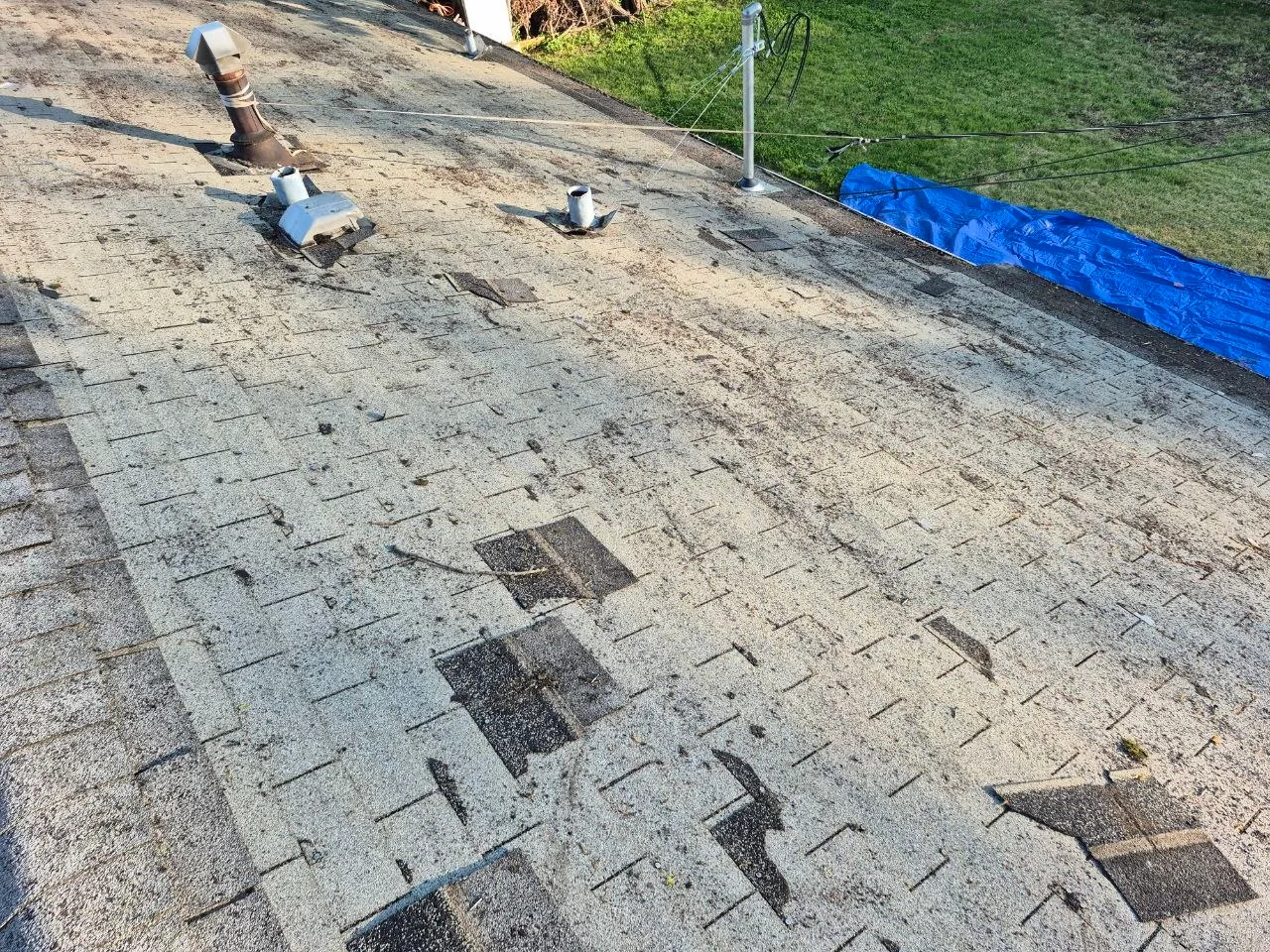 Severely damaged asphalt shingle roof in St. Louis showing missing shingles, granule loss, and exposed underlayment consistent with hail and storm damage.