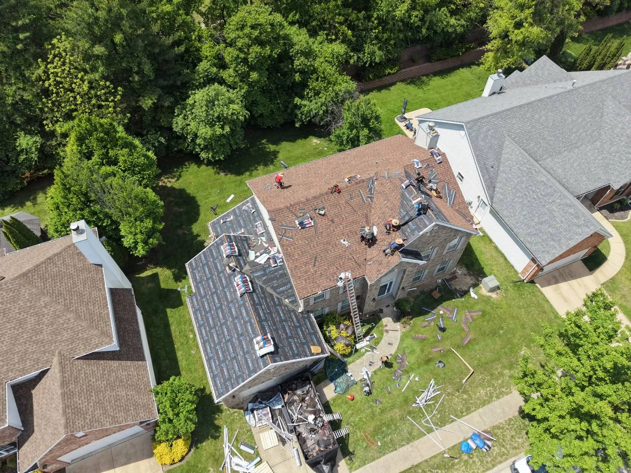Aerial drone view of St. Louis home mid-roof replacement with crew working on shingle installation.