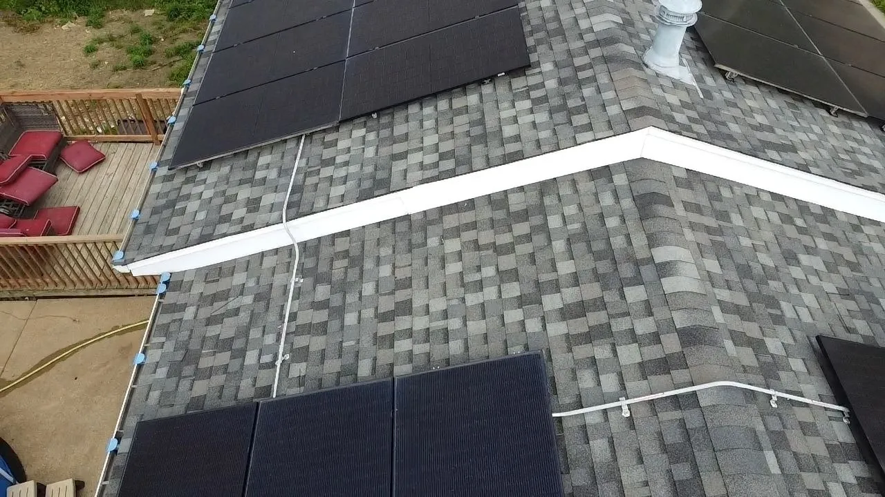 Aerial view of gray asphalt shingle roof with black solar panels and white conduit wiring in St. Louis, MO