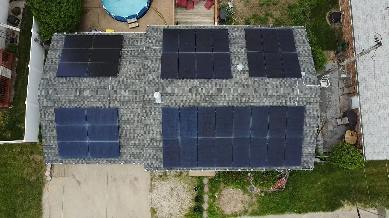Aerial drone view of residential home roof with multiple solar panel arrays installed on gray asphalt shingles.