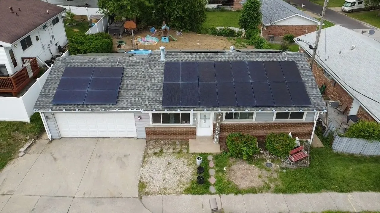 Aerial view of a single-story brick home in a residential neighborhood with solar panels installed across the roof.