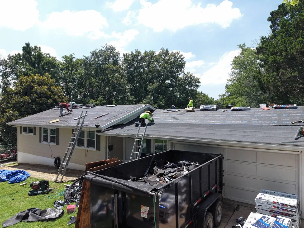 Roofing crew replacing shingles on a ranch-style home in St. Louis with dump trailer and materials on site.
