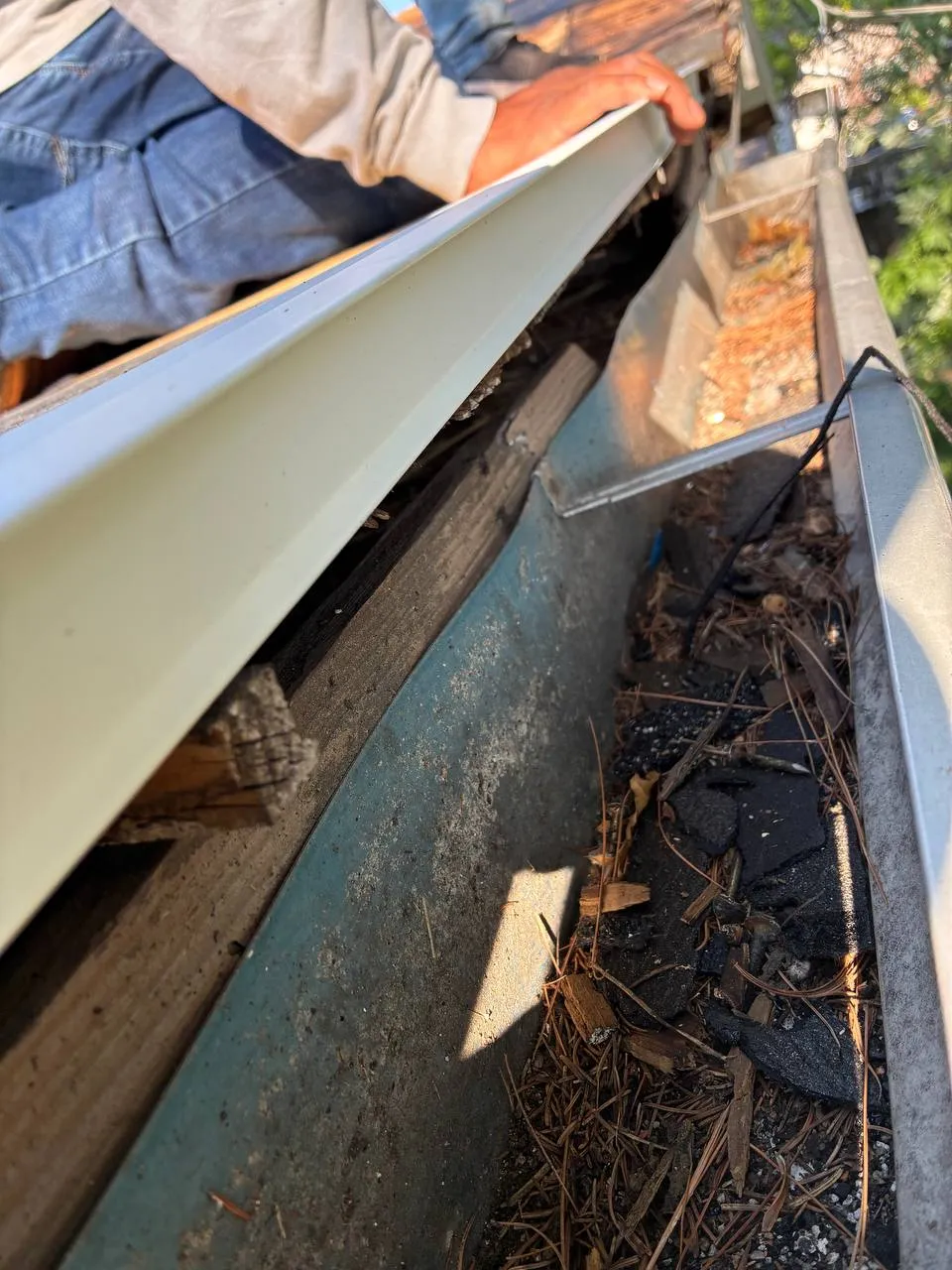 Roofer cleaning debris-filled gutters on a St. Louis home, removing leaves and buildup by hand.