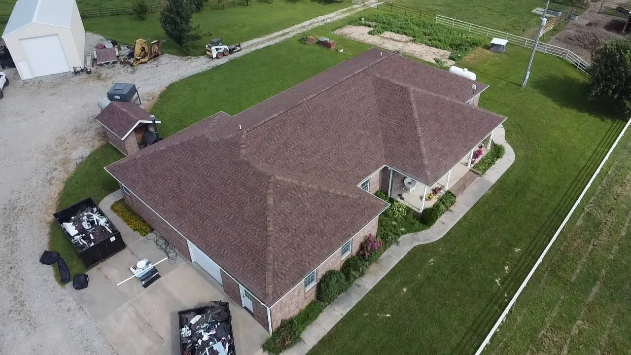 Aerial drone view of a brick ranch home with brown architectural shingle roof on a rural Missouri property