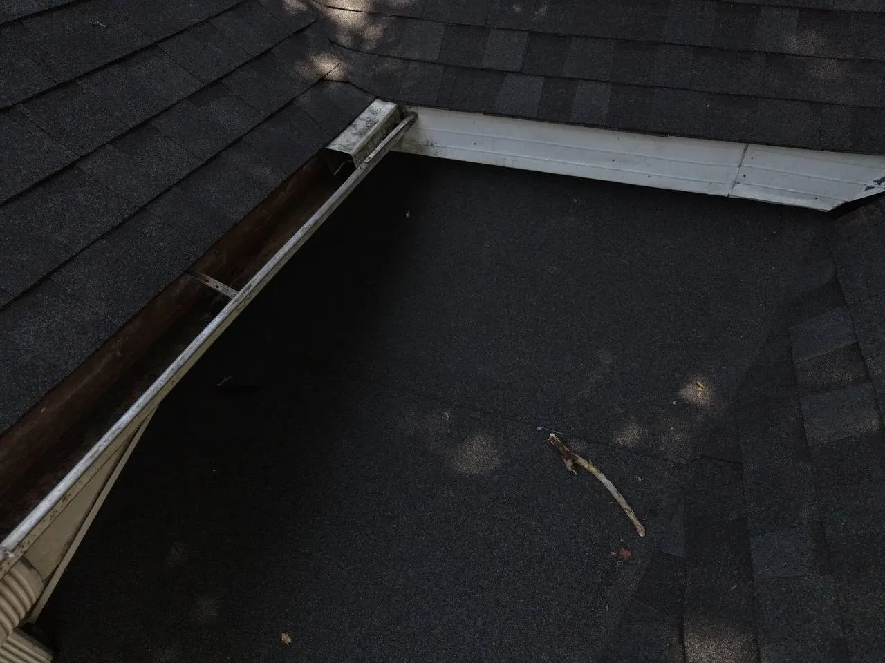 Close-up of a roof valley corner showing dark asphalt shingles, aluminum gutters, and white fascia trim in St. Louis home.