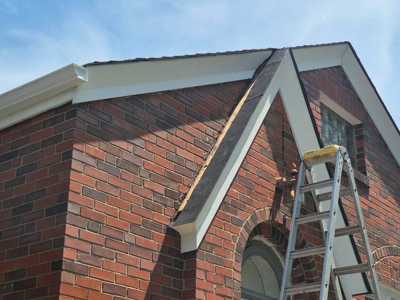 Brick building gable end repair with aluminum ladder and white fascia trim work in progress on St. Louis property