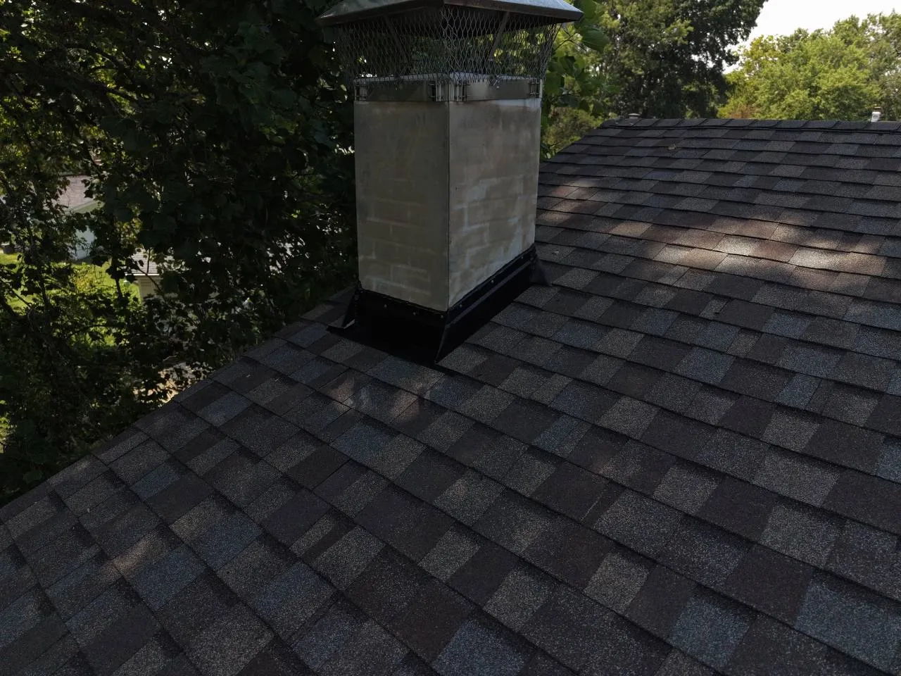Newly installed dark asphalt shingle roof with brick chimney and chimney cap in St. Louis, MO