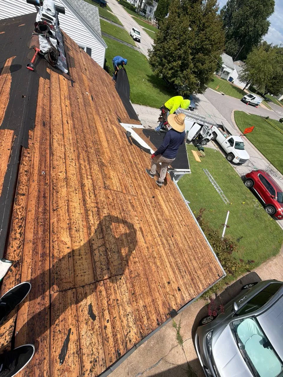 Roofing crew replacing shingles on a residential home in St. Louis, MO, with exposed wood decking visible.