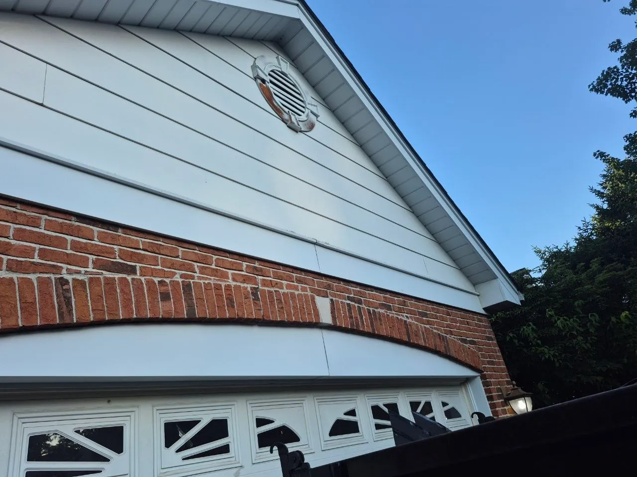 Close-up of white vinyl siding and red brick exterior on a garage with decorative white garage door in St. Louis