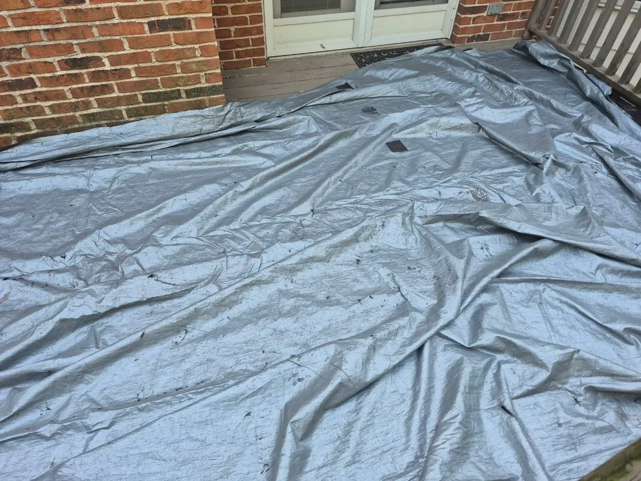 Silver tarp protecting a hail-damaged deck on a St. Louis brick home while a claim inspection is arranged.
