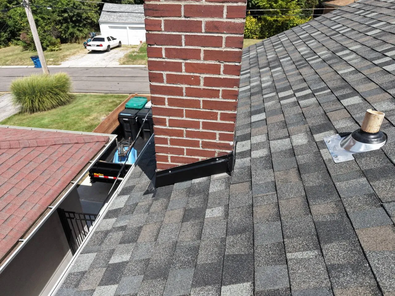 Gray architectural shingles on St. Louis home roof with brick chimney, step flashing, and plumbing vent boot.