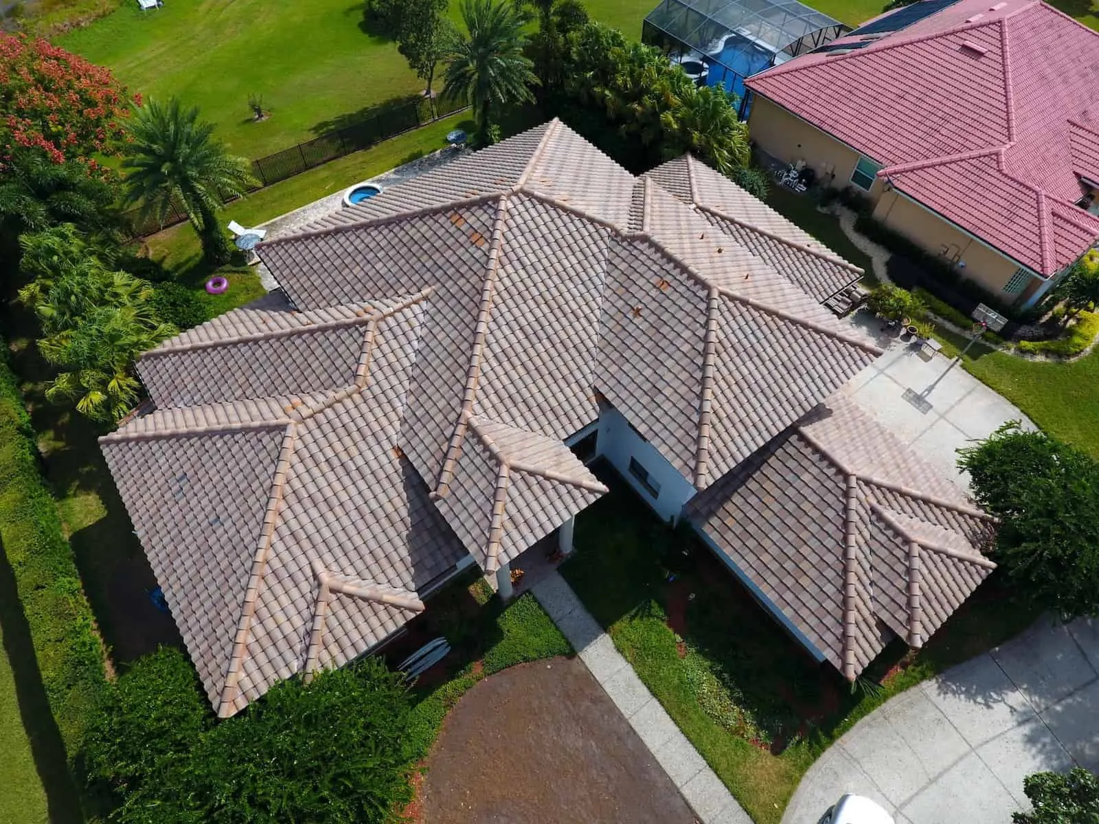 Aerial drone view of a large residential home with tan clay tile roofing in a Florida suburb.