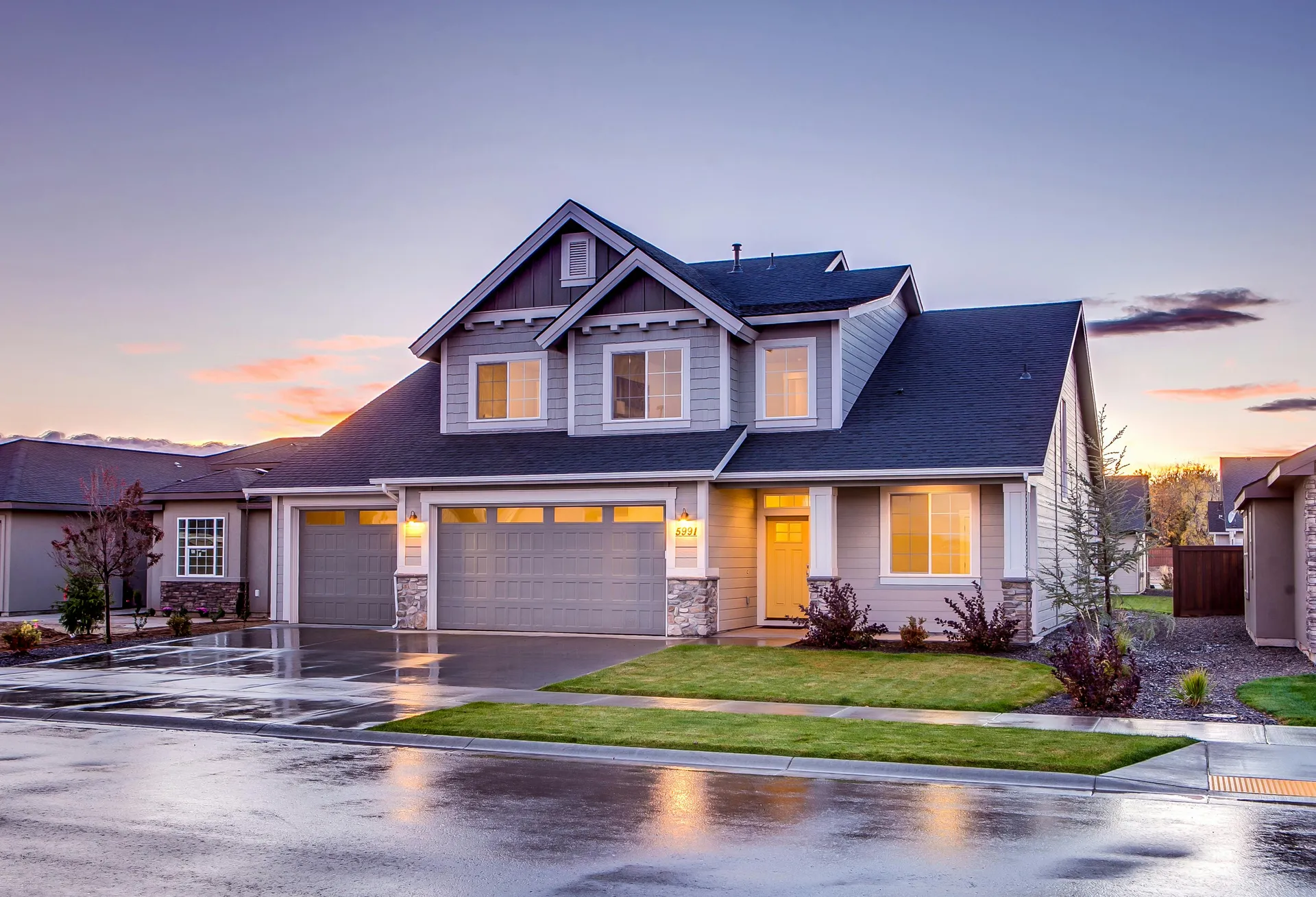 Two-story craftsman home with three-car garage and dark asphalt shingle roof at dusk in suburban neighborhood