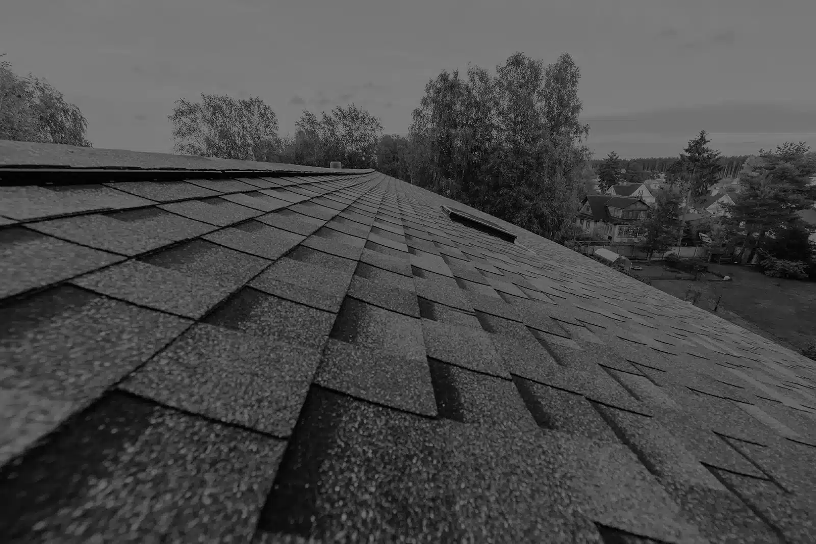 Close-up of gray asphalt shingle roof with suburban St. Louis neighborhood and trees visible in background.