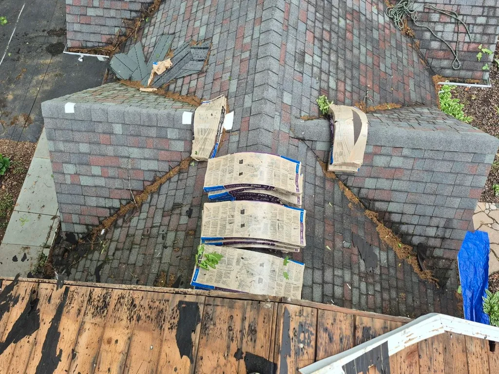 Aerial view of damaged asphalt shingle roof with stacked replacement shingles and debris in St. Louis, MO