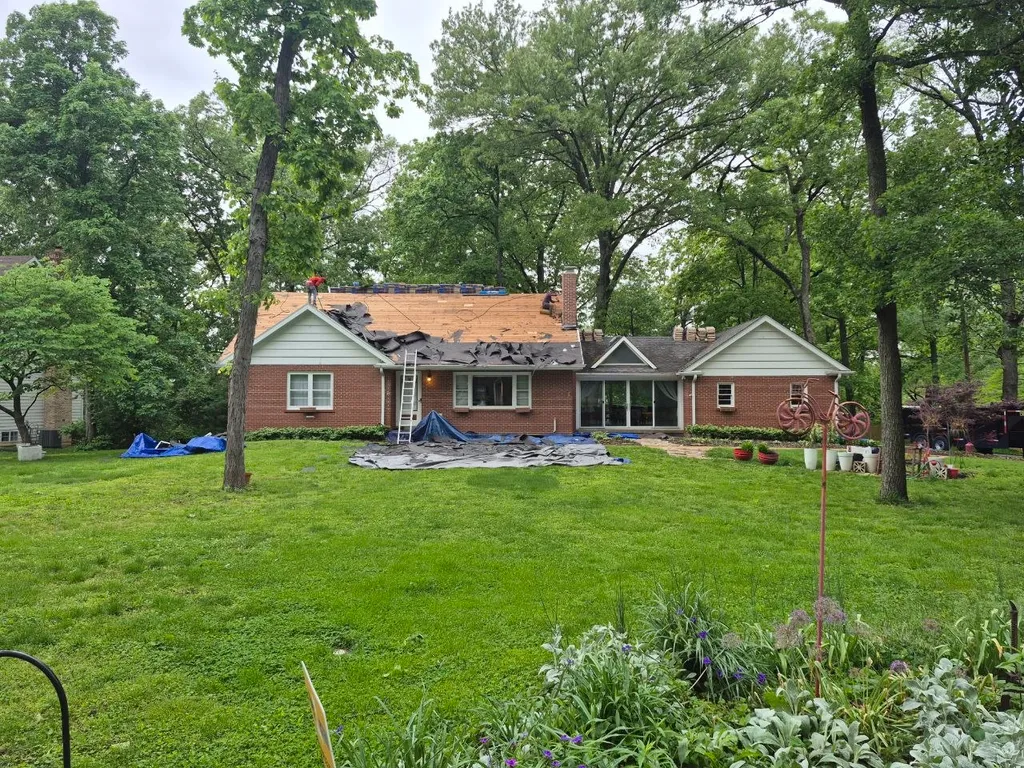 Roof tear-off in progress on a brick ranch home in St. Louis, with workers removing old shingles and exposing wood decking.
