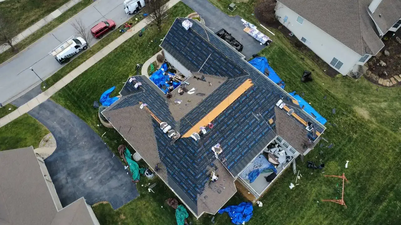 Aerial drone view of a residential roof replacement in progress with blue underlayment and partial shingles installed.