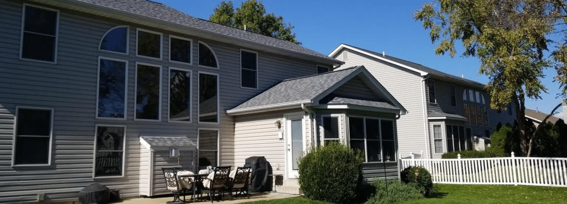 Two-story home with gray vinyl siding, arched windows, screened porch addition, and asphalt shingle roof on sunny day.