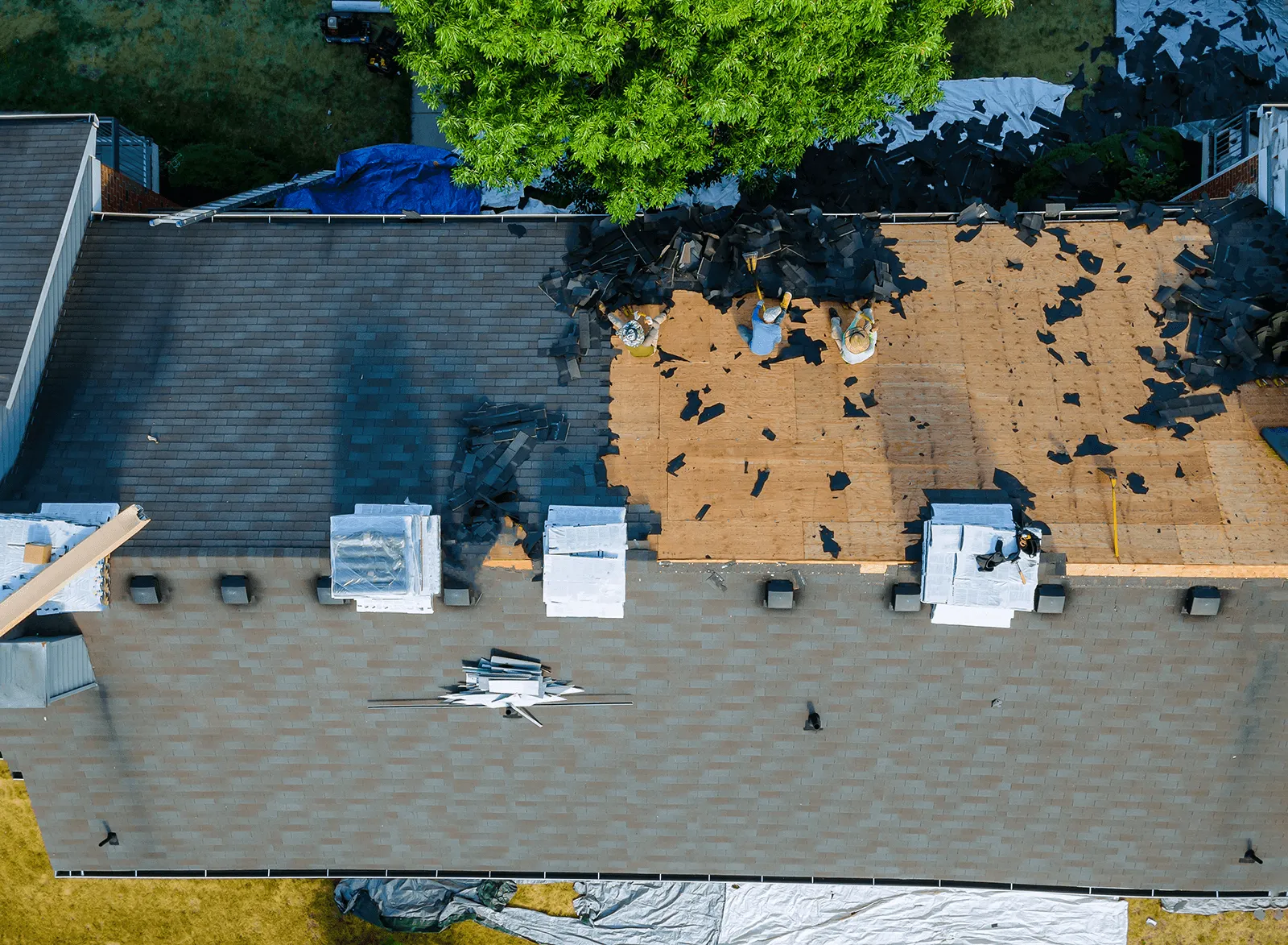 Aerial drone view of residential roof replacement in progress, showing stripped decking and workers in St. Louis, MO