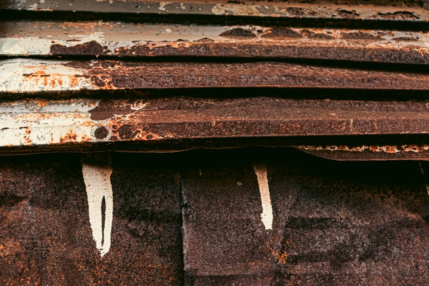 Severely rusted and deteriorating metal roof panels with peeling white paint and corrosion damage