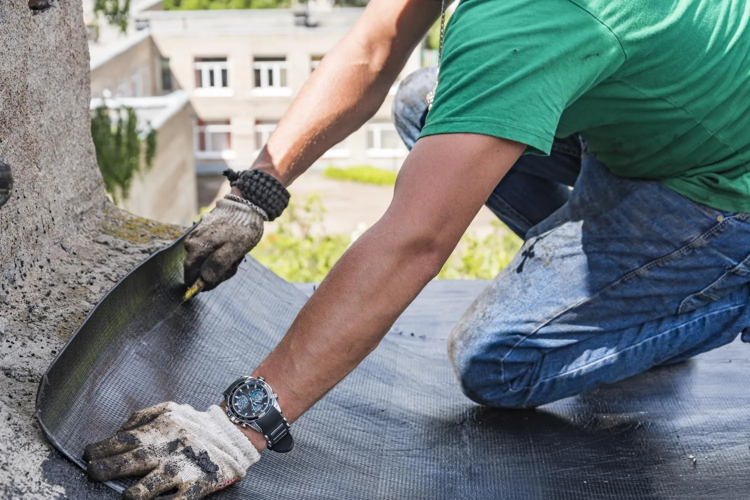 Roofer in green shirt installing waterproofing membrane on flat roof in St. Louis